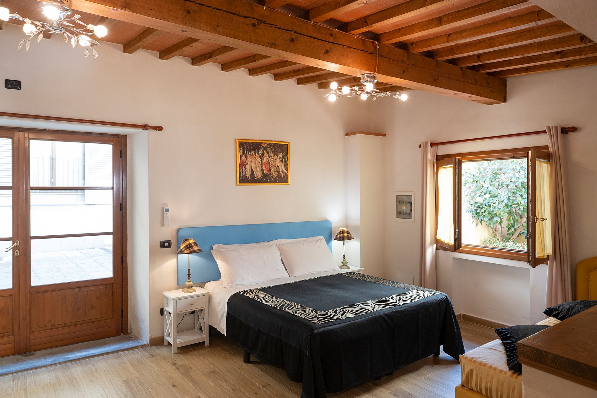 Bright bedroom with wooden ceiling, blue bedspread, and sunlight through windows