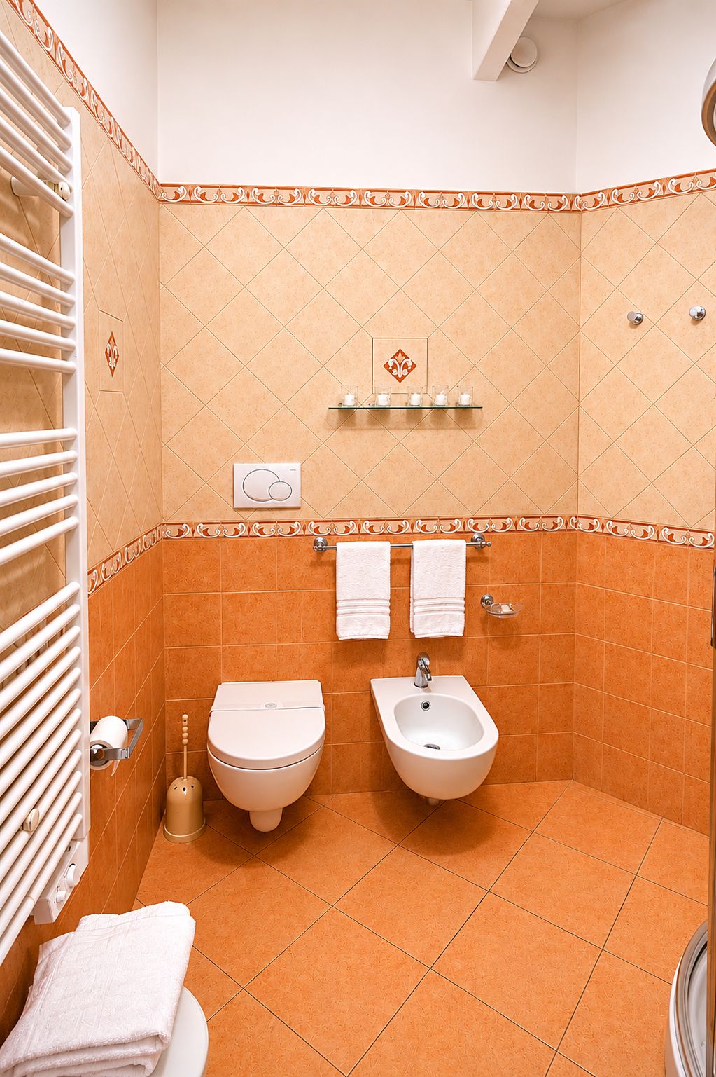 Small tiled bathroom with toilet, bidet, towel radiator, and white towels