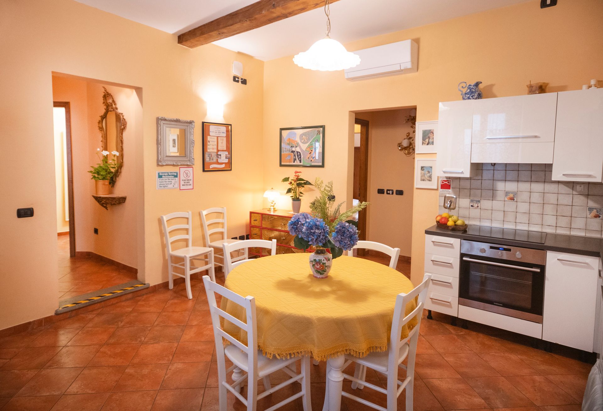 Cozy kitchen with round yellow table, white chairs, tiled floor, and white cabinets in warm orange walls