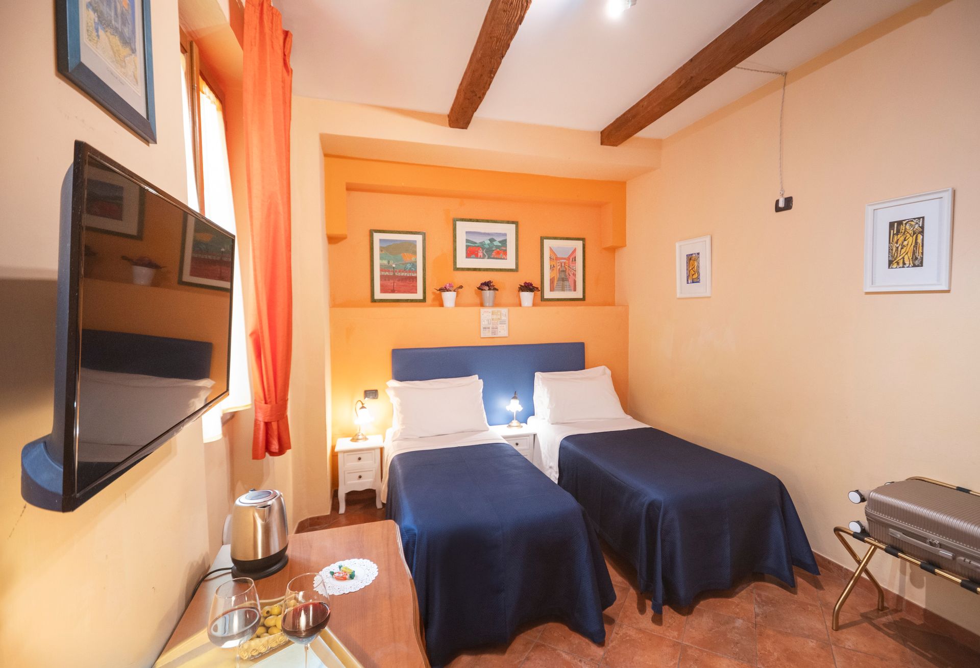Cozy bedroom with two twin beds, blue bedding, warm orange walls, and a wall-mounted TV