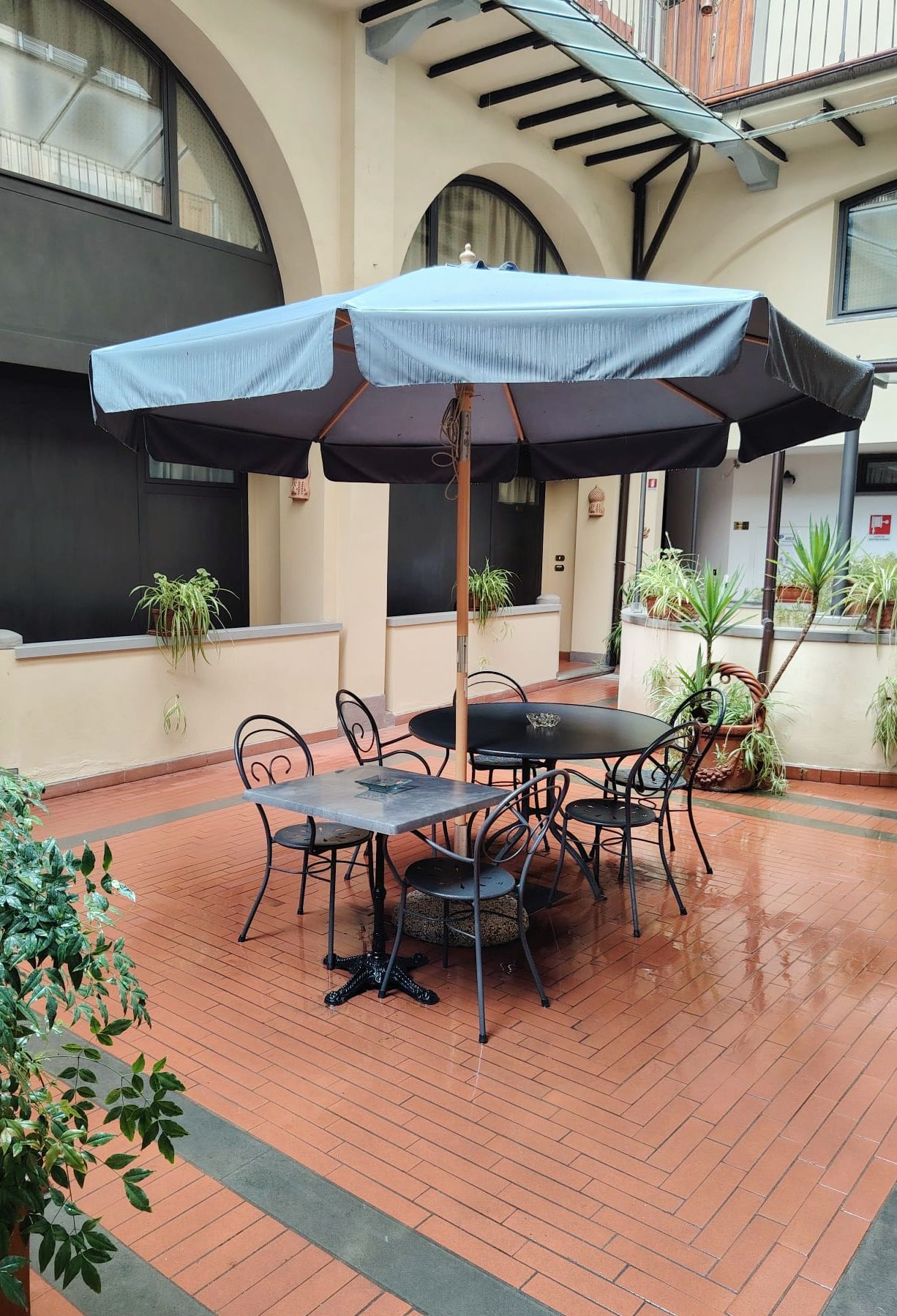 Outdoor patio with black table, chairs, and a large gray umbrella on brick paving