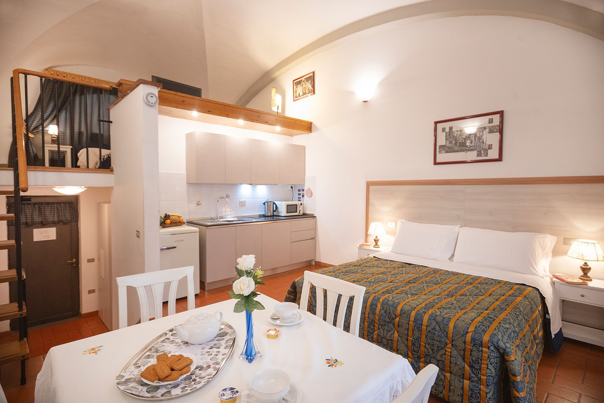 Cozy studio apartment with loft bed, kitchenette, dining table, and single bed by a window-lit wall