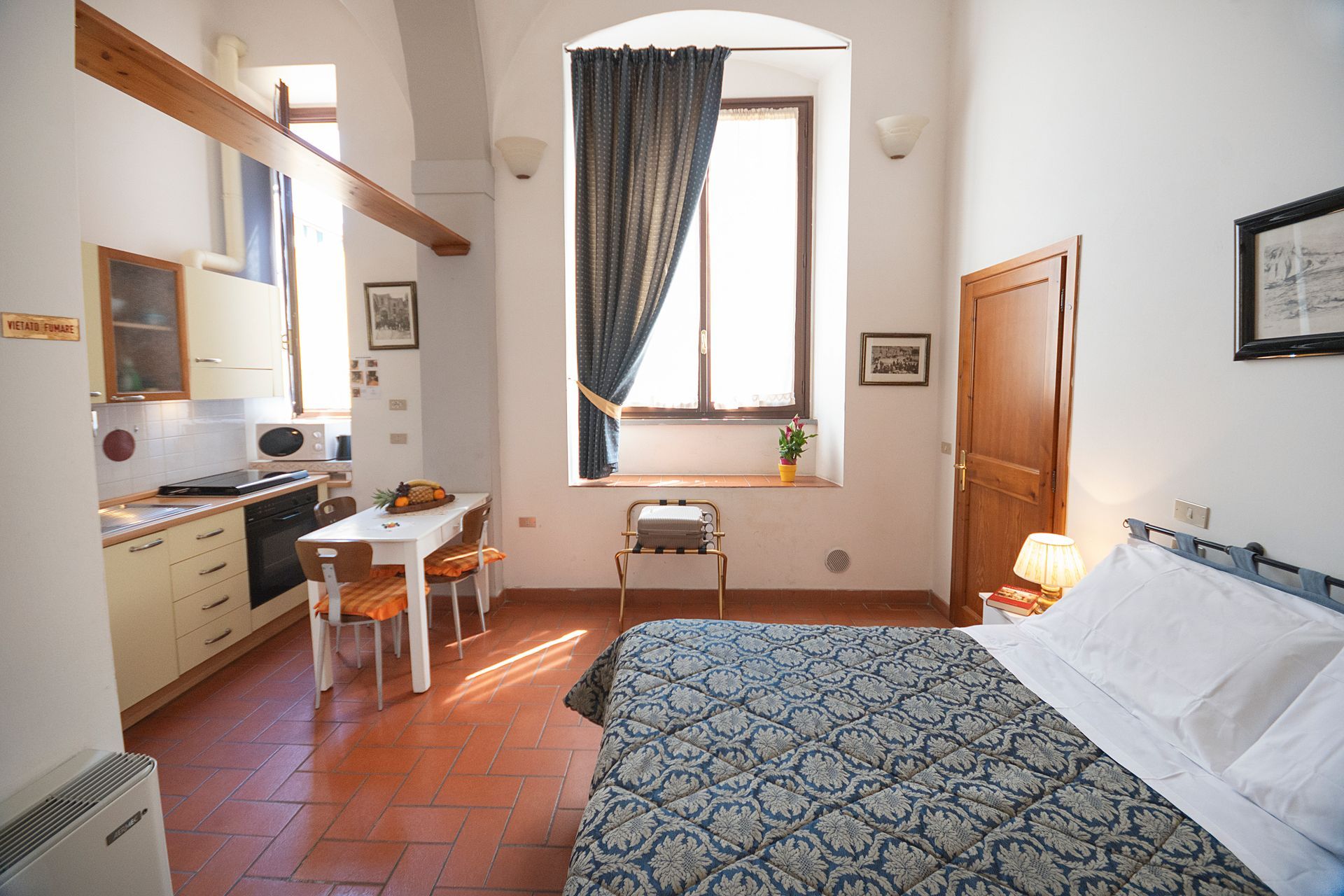 Bright bedroom with bed, desk, window, terracotta floor, and white walls