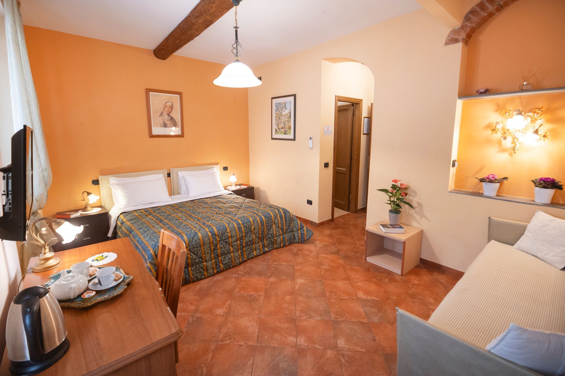 Cozy bedroom with a double bed, terracotta tile floor, wood beams, and warm wall lighting.