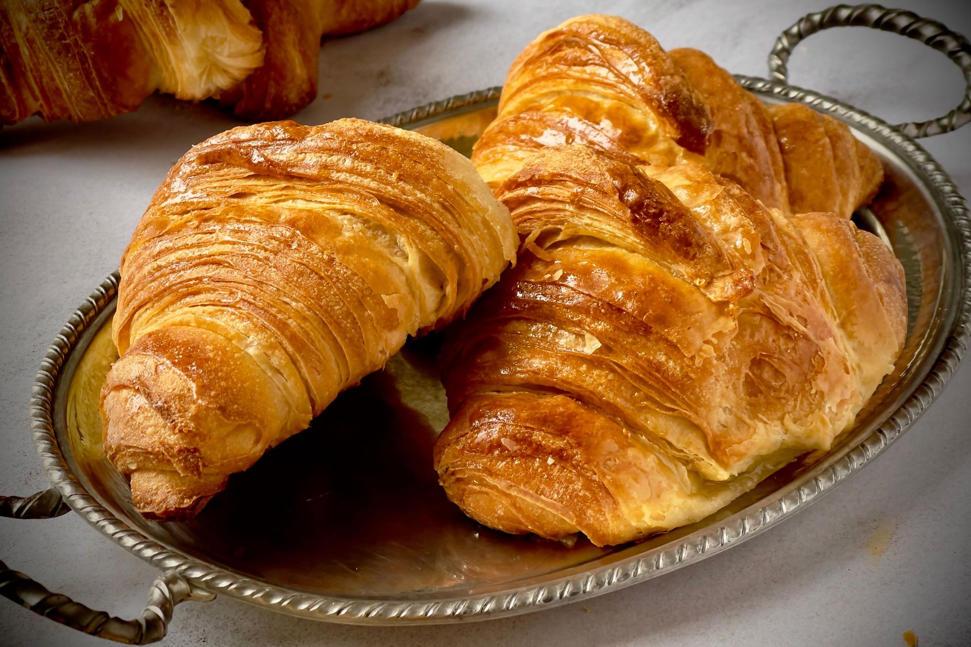Two golden-brown croissants on an ornate silver tray