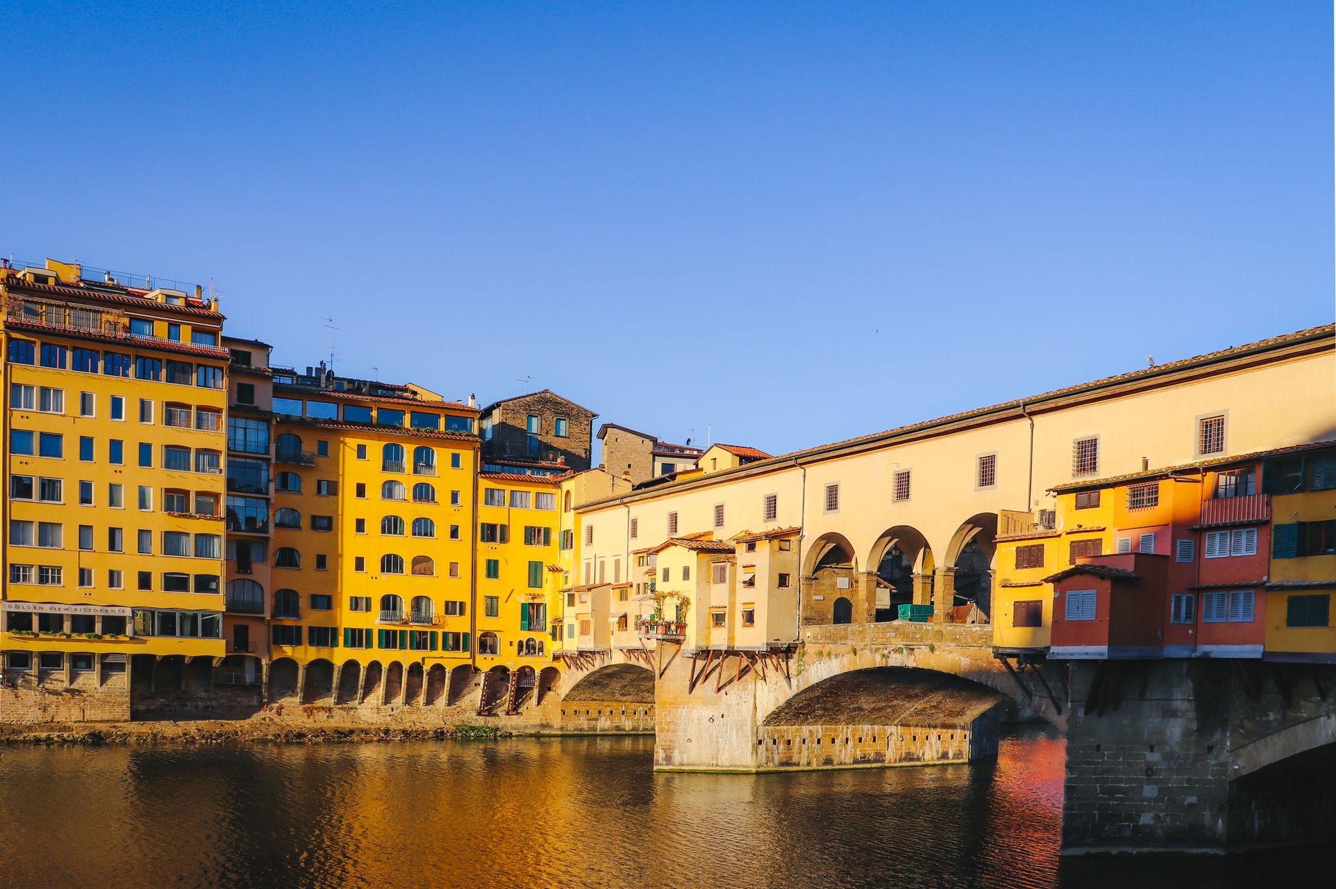 Colorful buildings and a stone bridge over a river at sunset in a European town