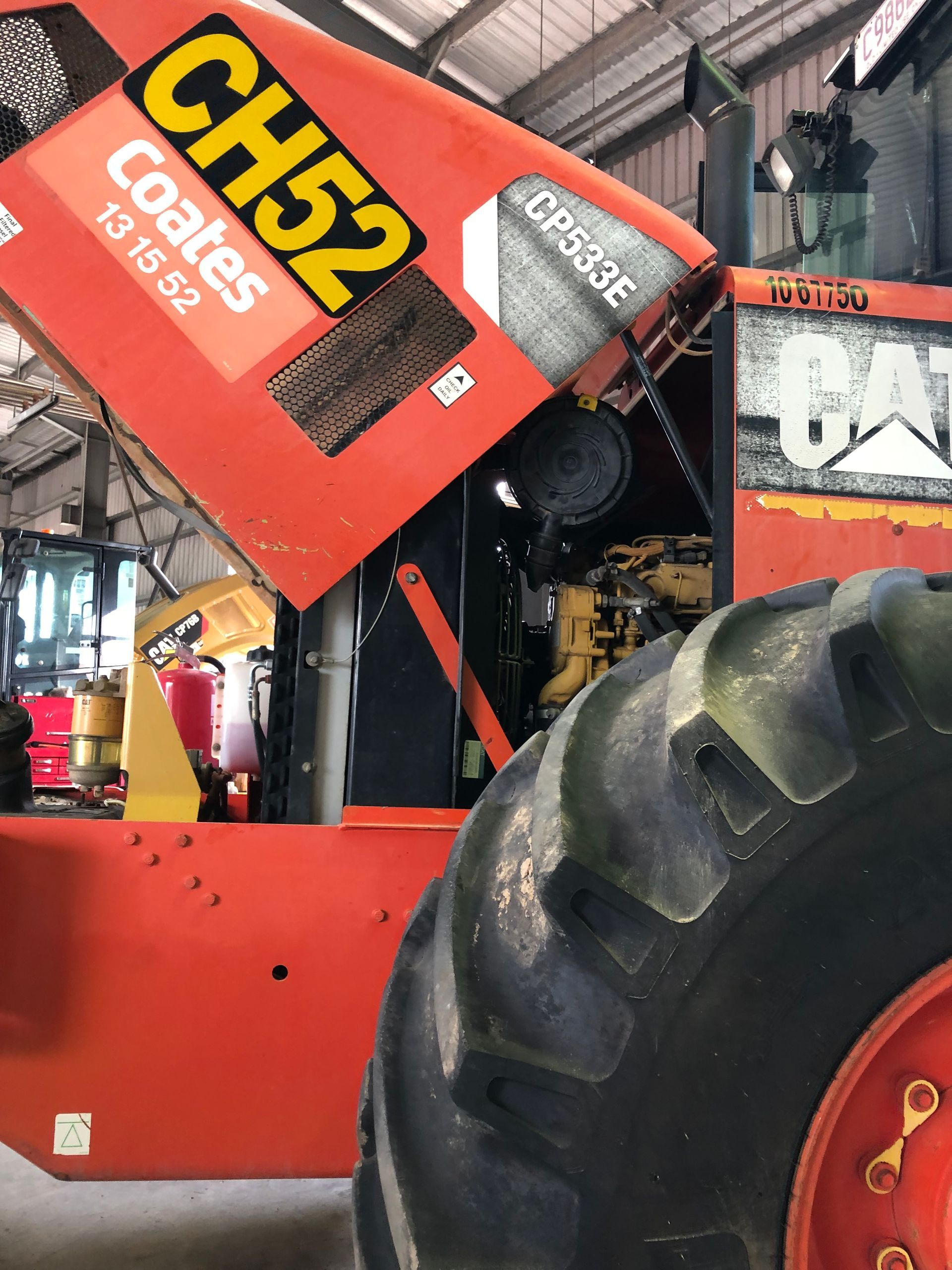 Orange industrial machine with raised hood, partially obscuring the engine; black tire in the foreground. — Bodes All Mechanical In Tathra, NSW