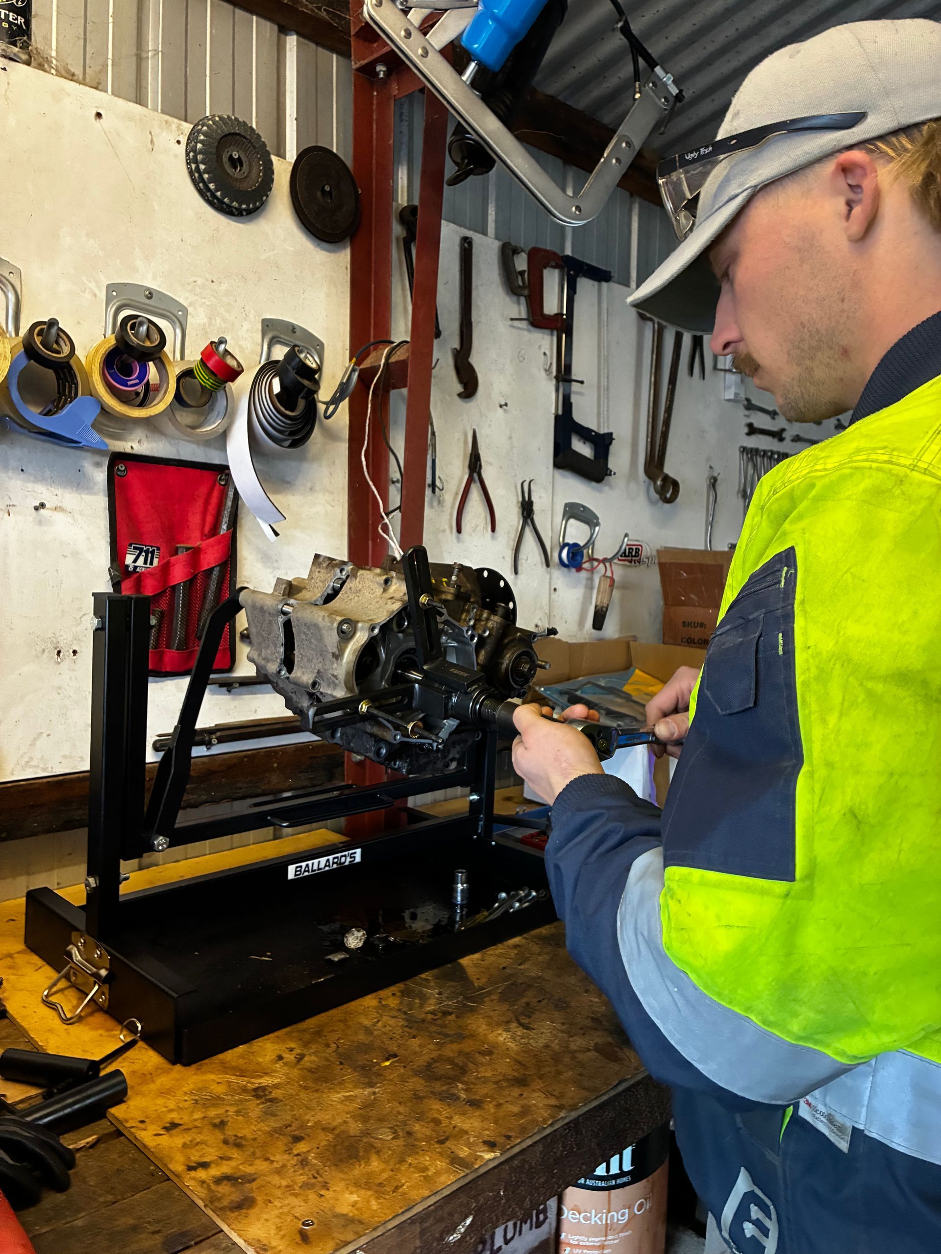 Mechanic working on an engine mounted on a stand in a workshop, wearing a safety vest. — Bodes All Mechanical In Pambula, NSW