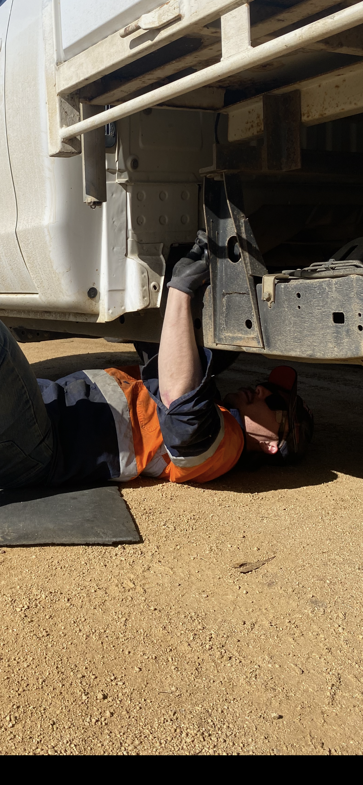 A Mechanic Wearing Safety Gear Working Under a Vehicle on Gravel — Bodes All Mechanical In Pambula, NSW