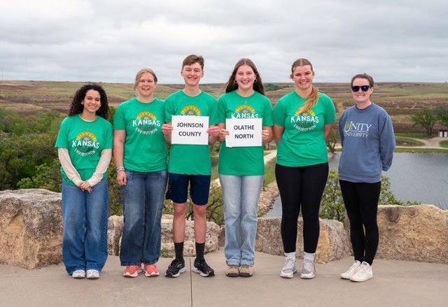 Group of students wearing matching shirts, standing outside in an open prairie