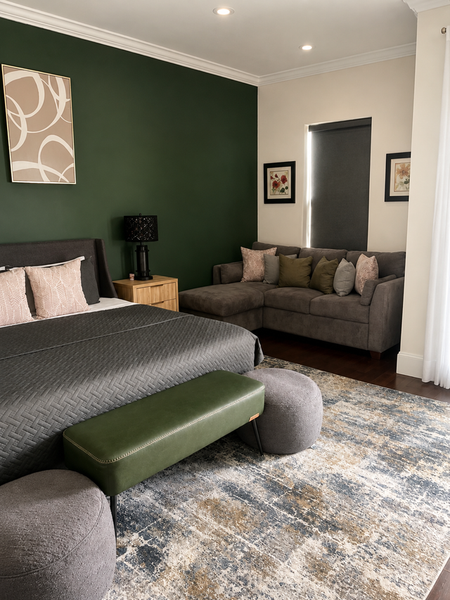 Bedroom with gray bed, green accent wall, sofa, and patterned rug
