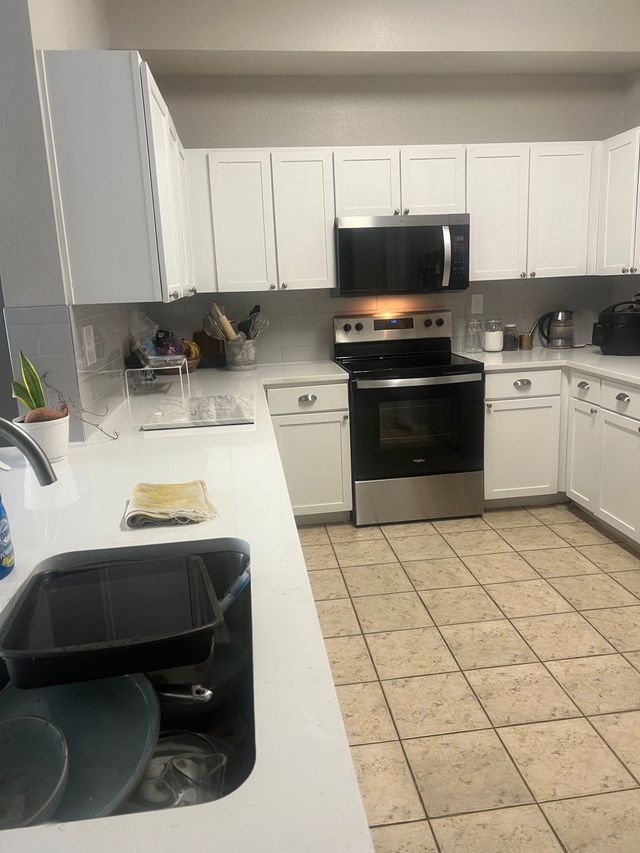 White kitchen with black appliances, tiled floor, and a white countertop sink in the foreground.