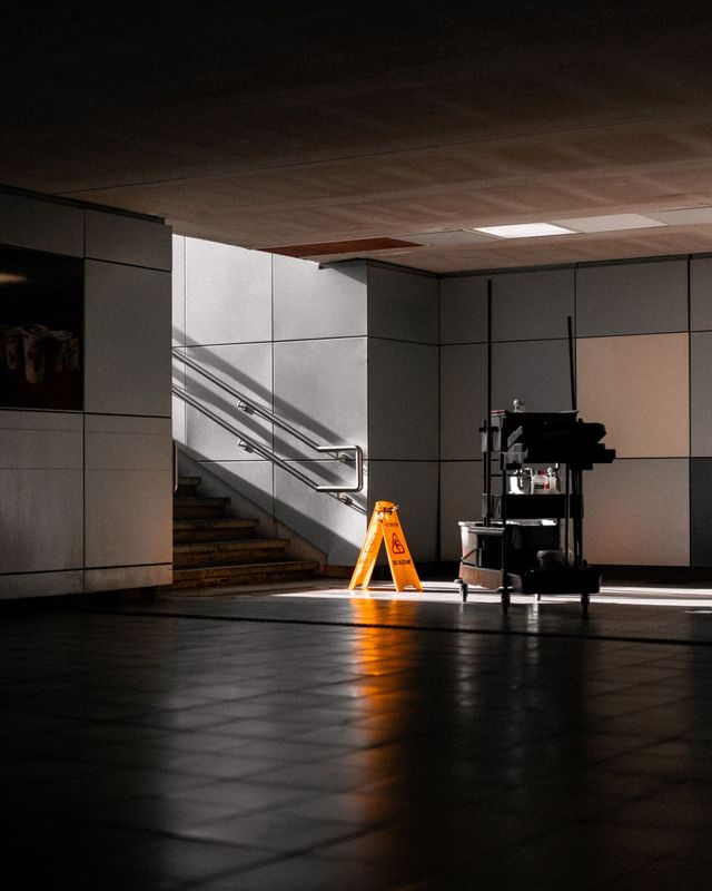 Dim indoor lobby with stairs, bright orange caution sign, and reflected light on a dark tiled floor