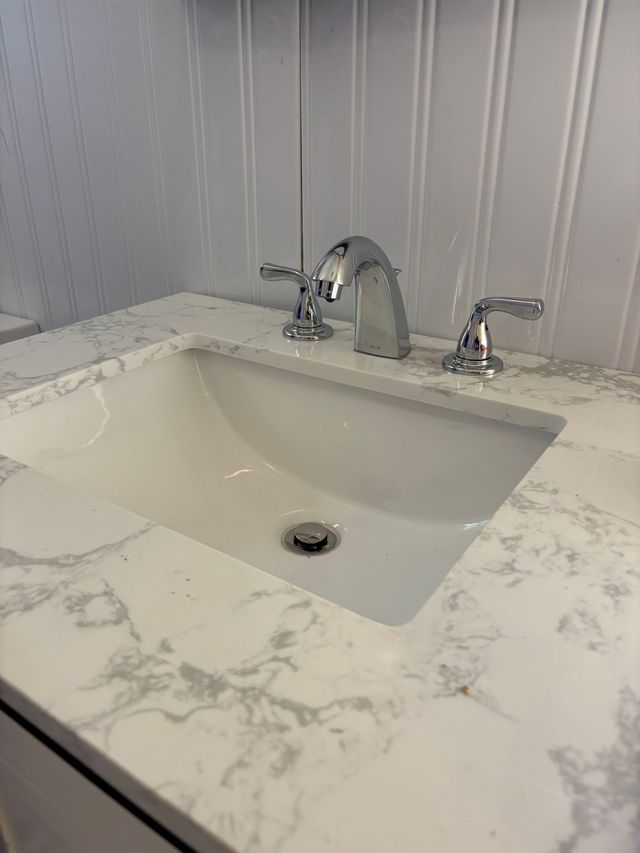 Bathroom sink with marble countertop, chrome faucet, and gray paneled wall backsplash.