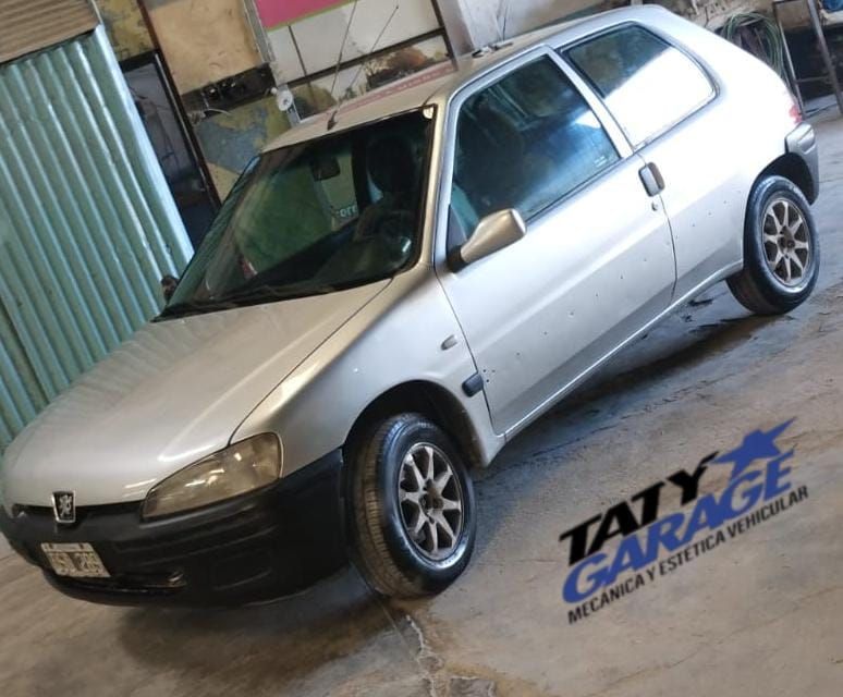 Peugeot 106 plateado aparcado en un garaje, logotipo de Taty Garage visible.