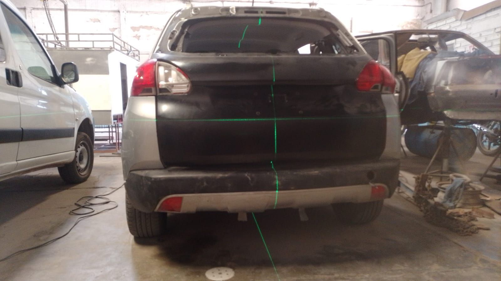 Vista trasera de un SUV plateado y negro en un taller de reparación, con líneas láser verdes a lo largo de la carrocería.