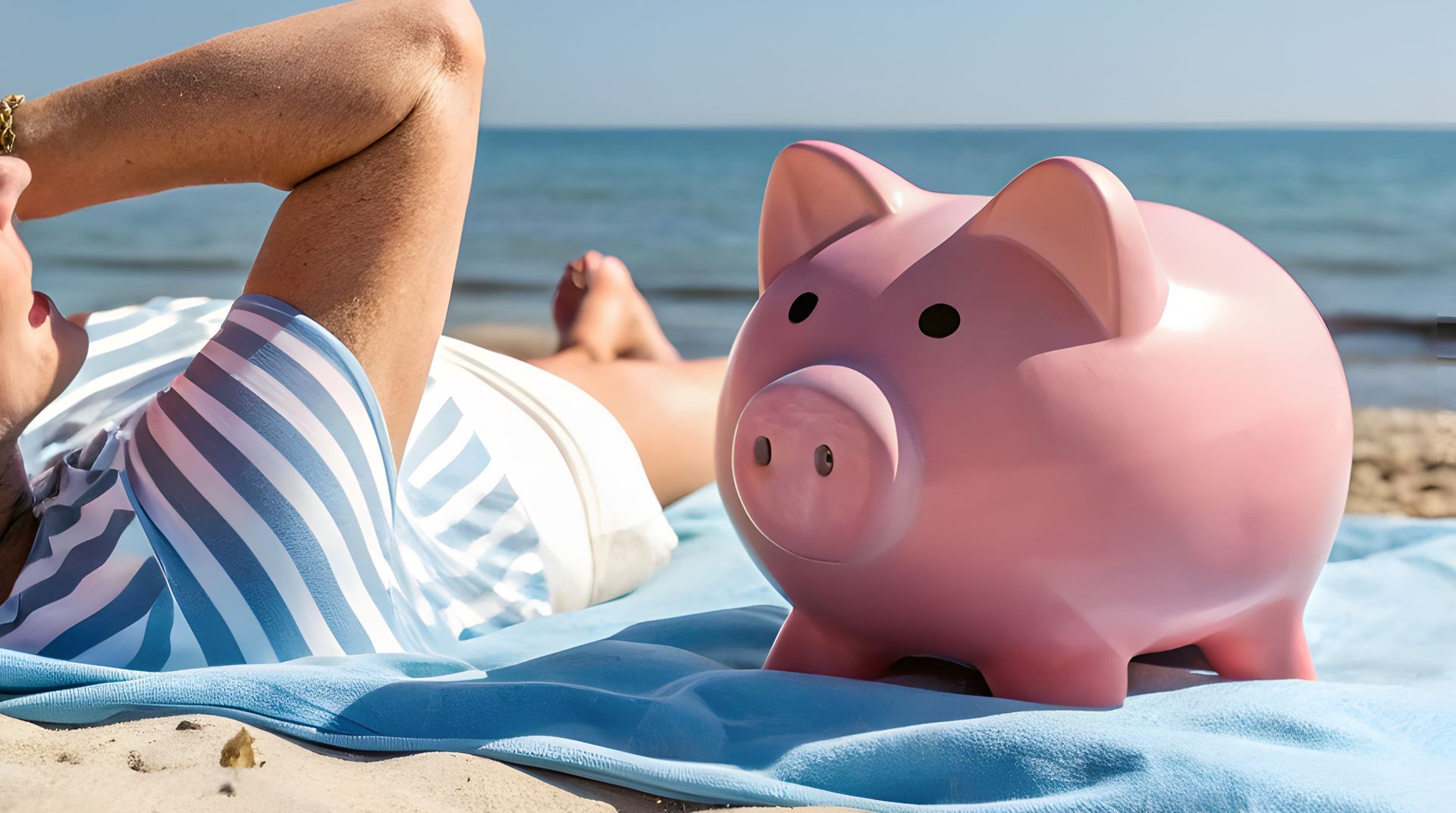 A woman is laying on the beach next to a pink piggy bank.