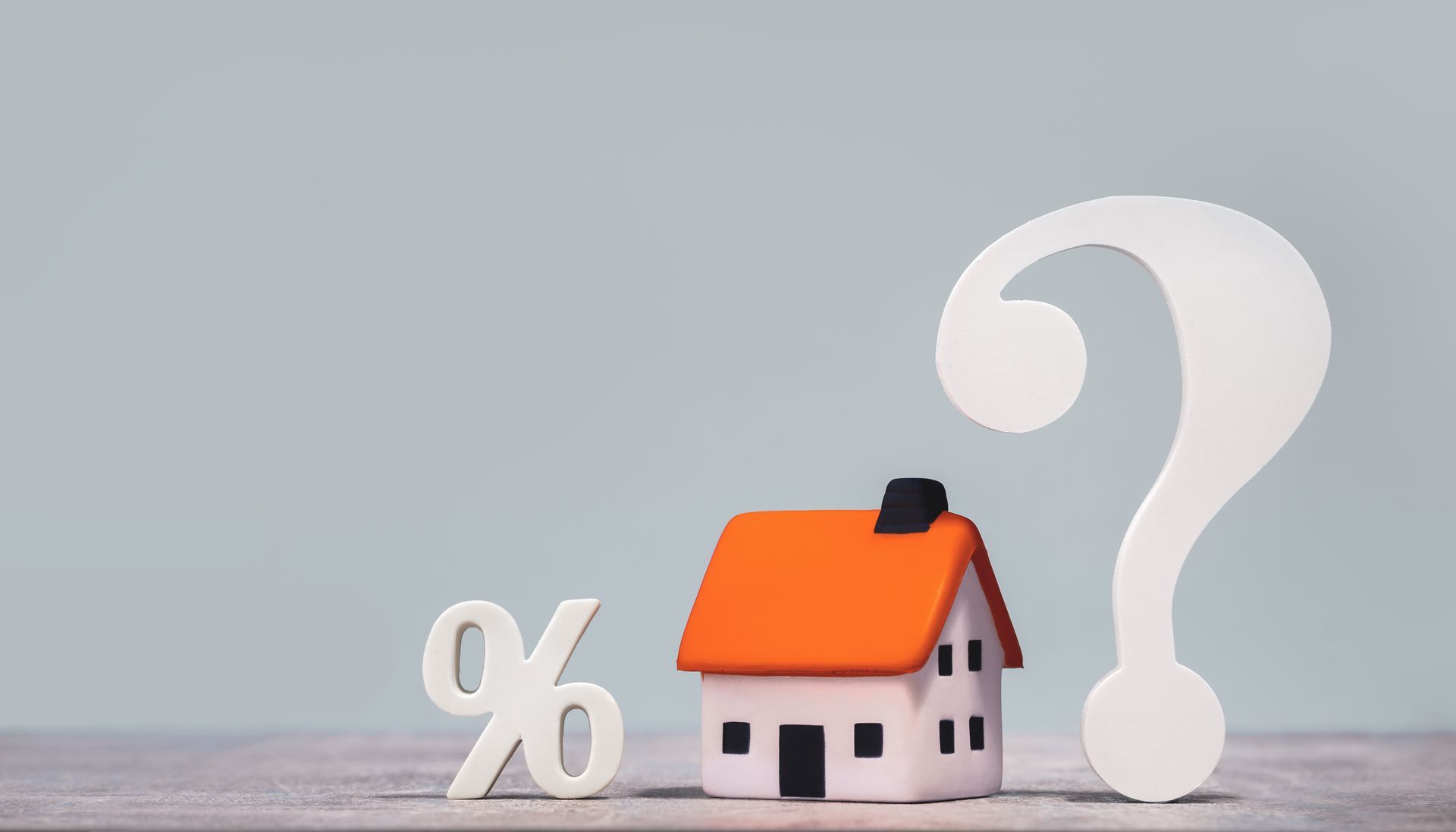 A small house, a percentage sign, and a question mark on a light blue background, representing real estate and interest rates.