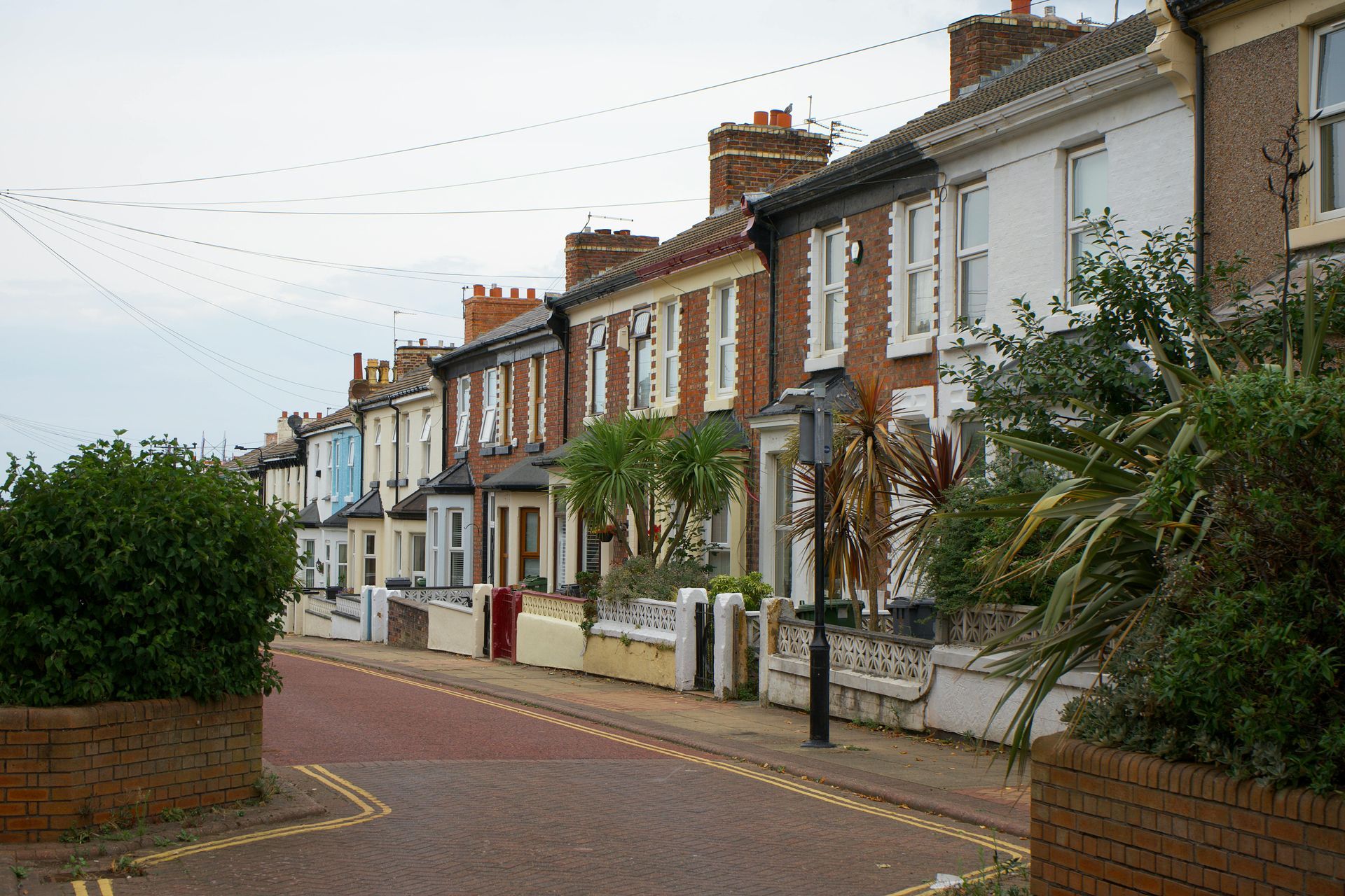 Row of colourful brick houses along a brick street, overcast sky.