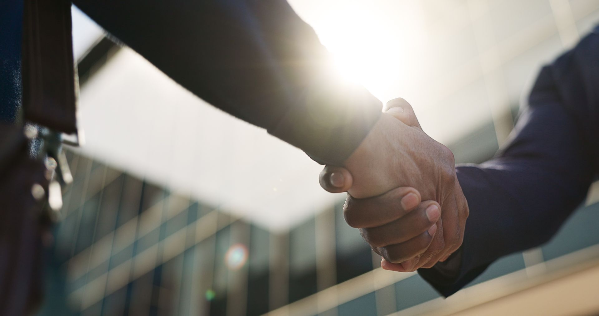 Two men are shaking hands in front of a building.