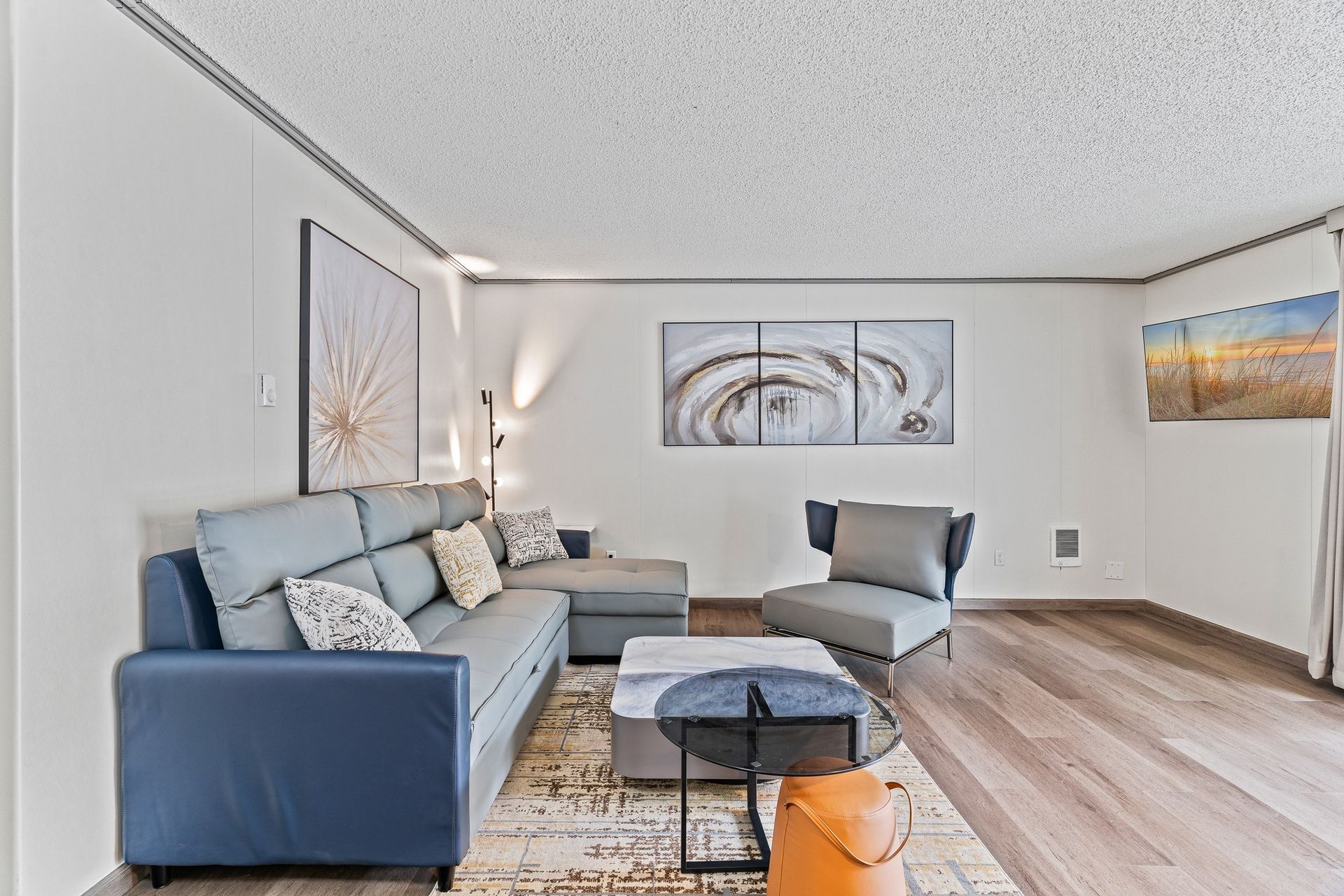 A living room with a couch , chair , coffee table and paintings on the wall.