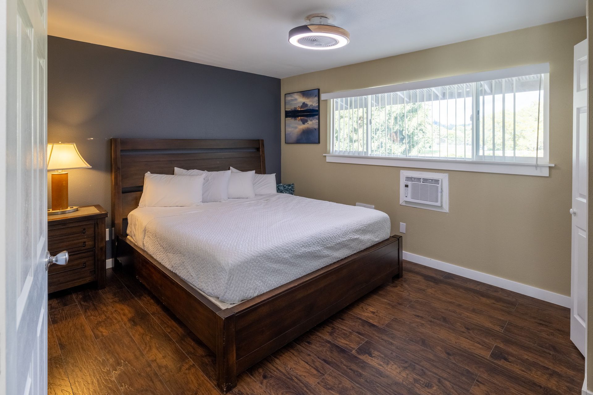 A bedroom with a king size bed , nightstand , lamp and window.