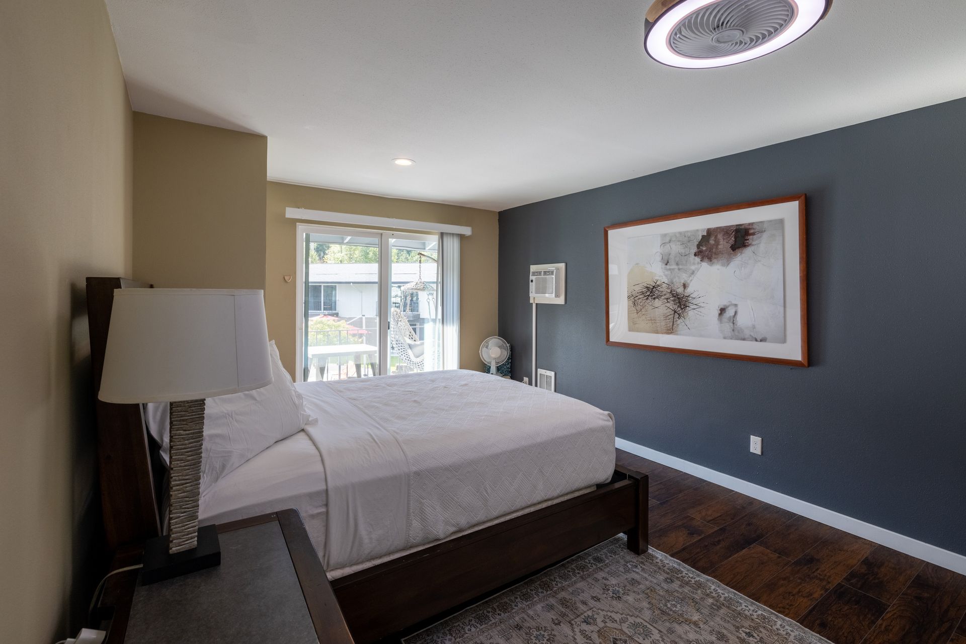 A bedroom with a bed , nightstand , lamp and a picture on the wall.
