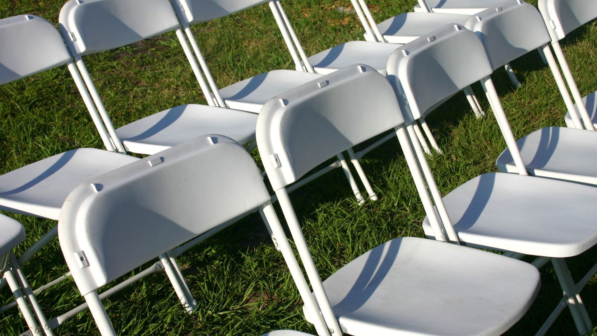 a row of white folding chairs in the grass