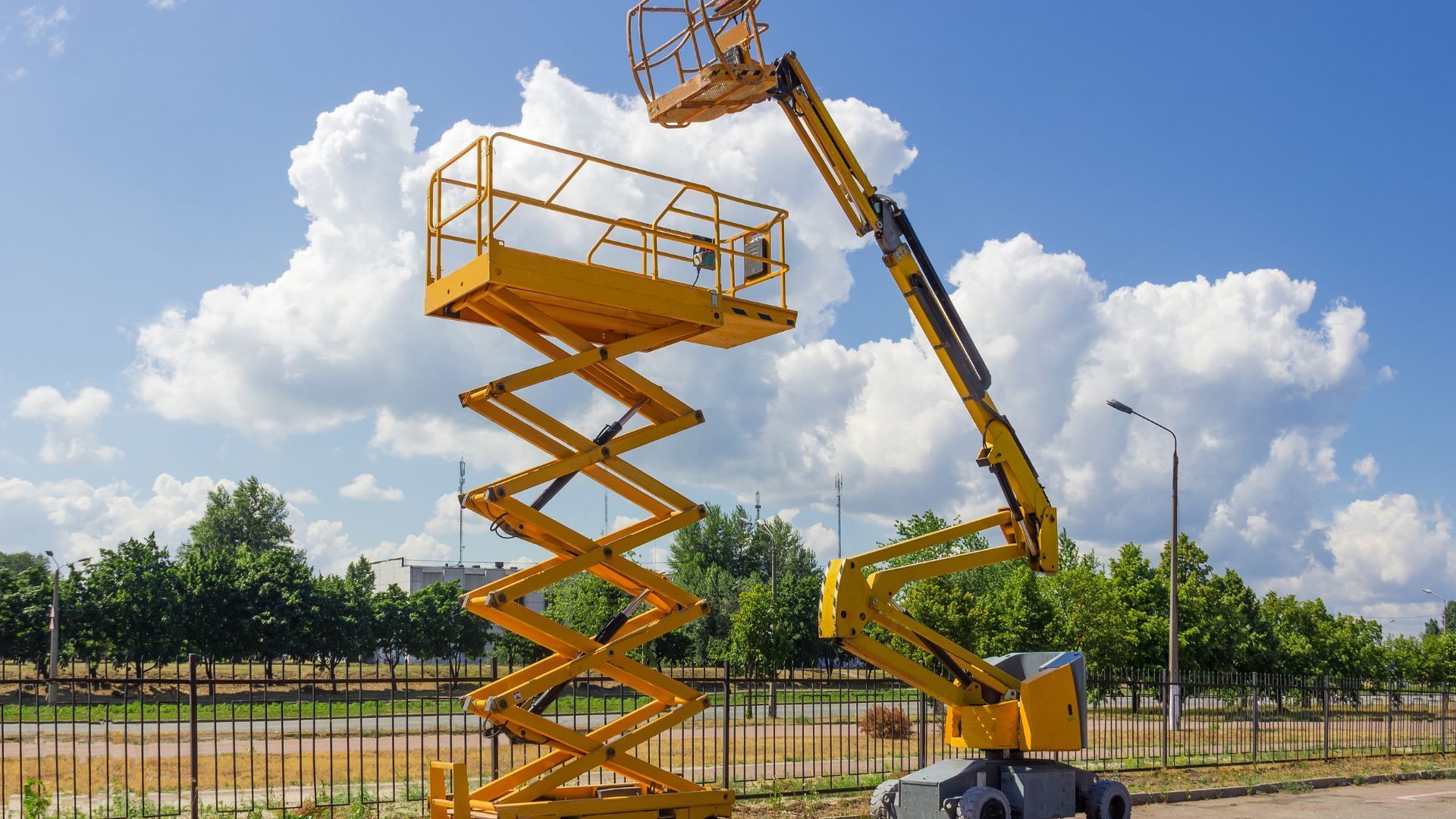 a yellow scissor lift is sitting on top of a fence in a parking lot .