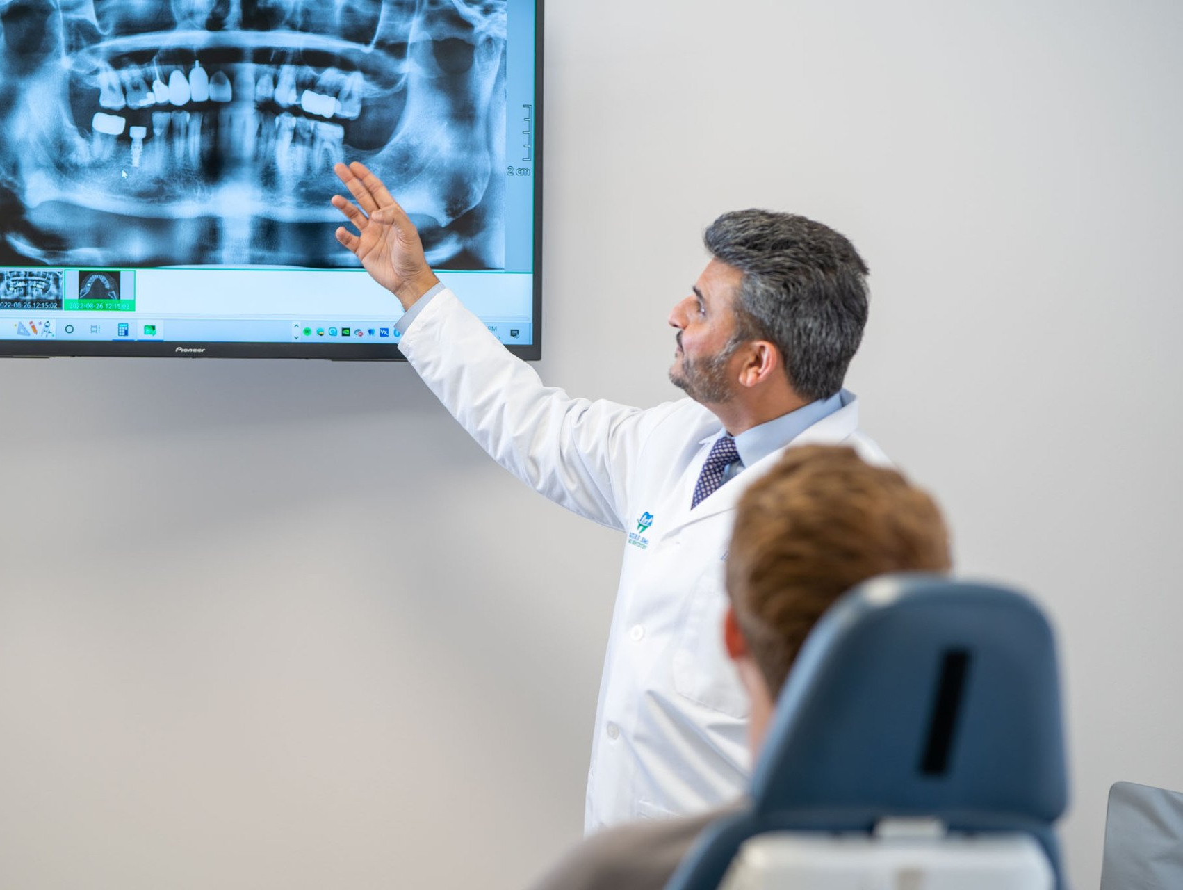 Dentist pointing at a jaw X-ray on a wall monitor in a clinic