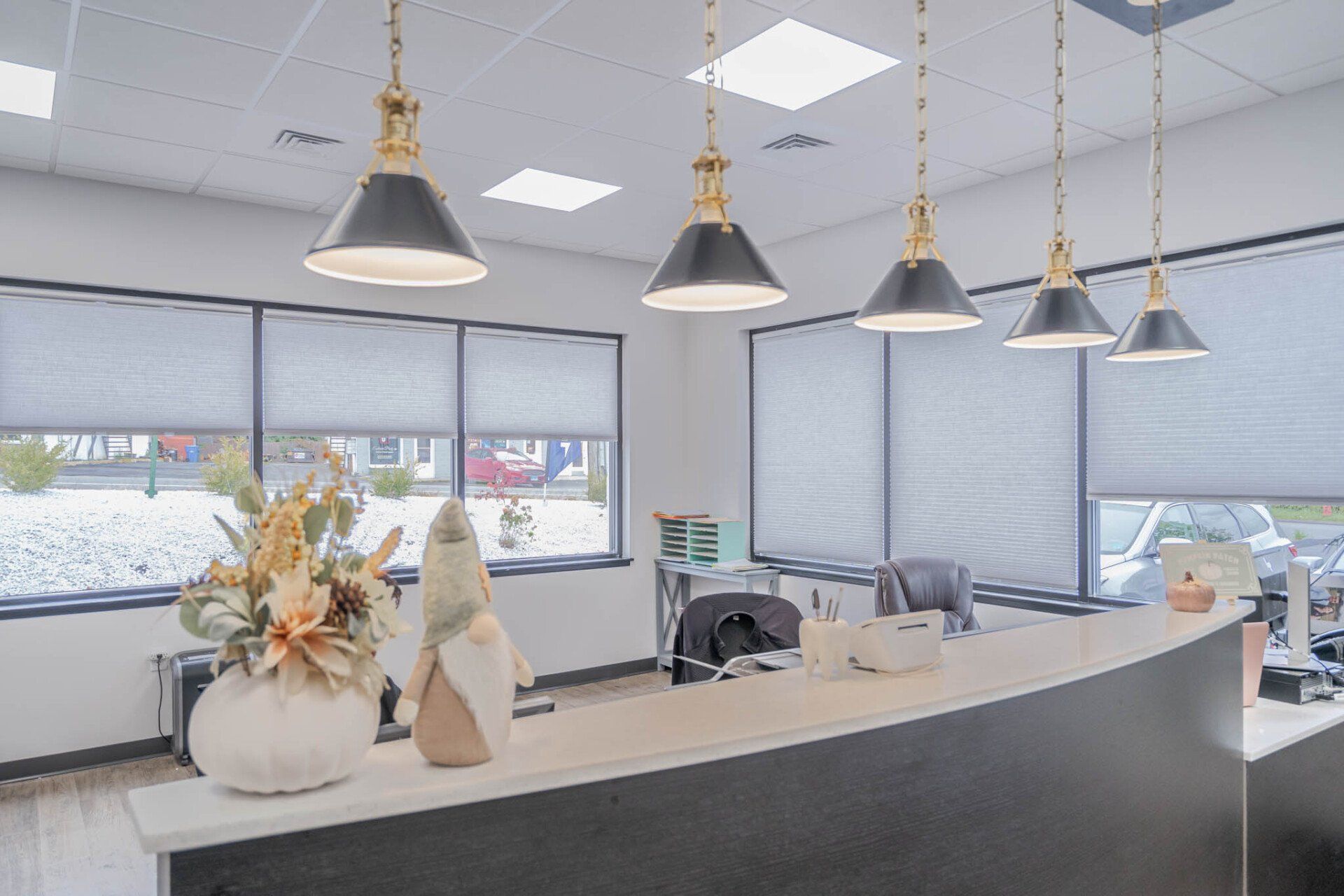 Bright office reception desk with pendant lights, large windows, and white blinds.