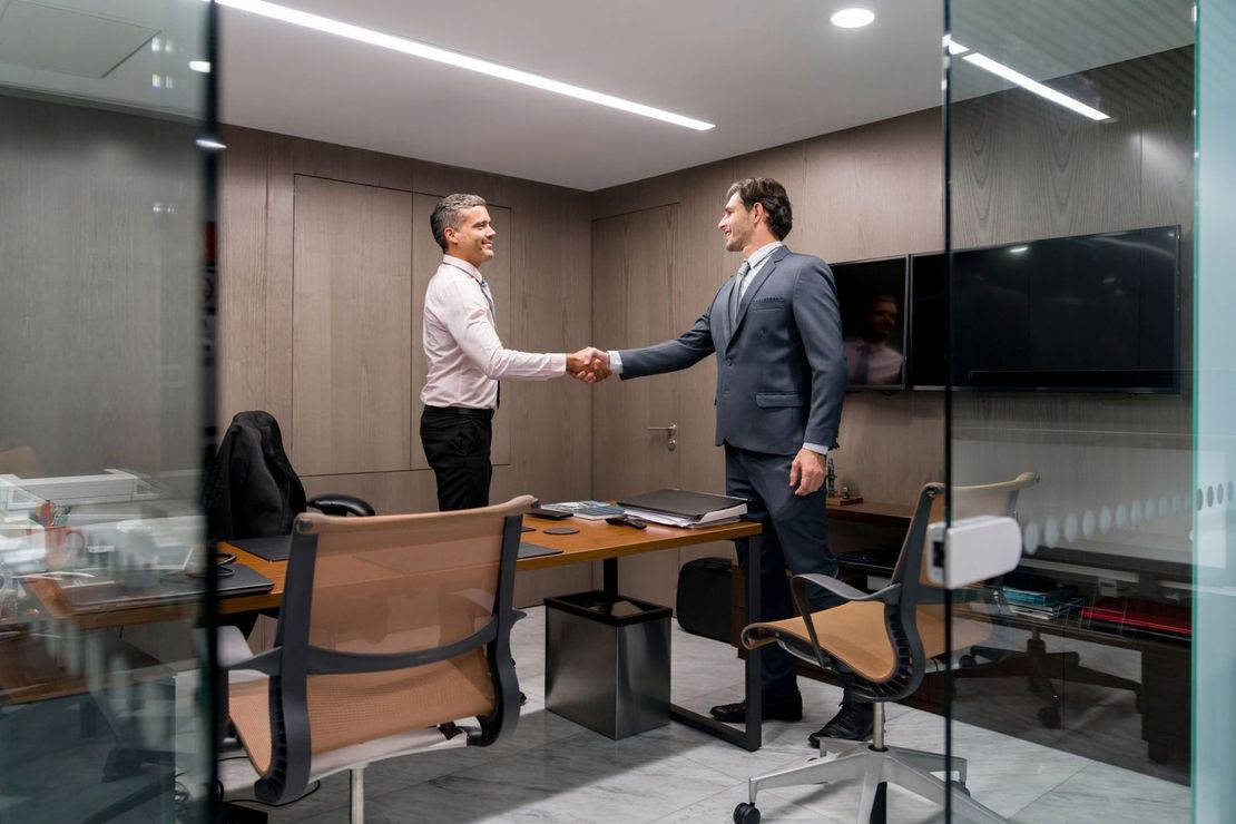 Two people shaking hands in an office, smiling.