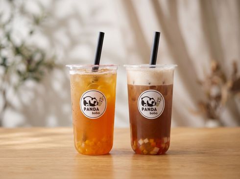Two iced drinks with black straws on a wooden table, one orange and one brown, in branded cups