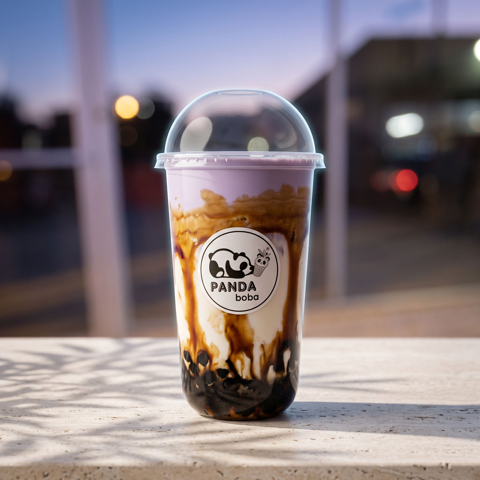 Panda-branded bubble tea with dark tapioca pearls in a clear cup on a table at dusk