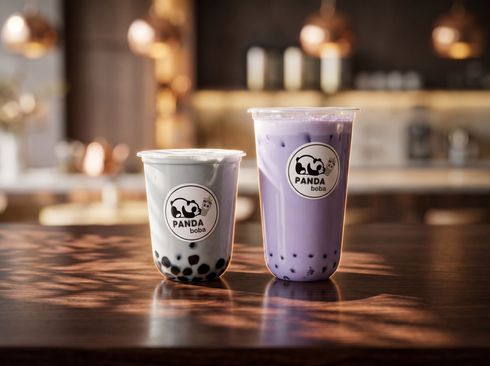 Two bubble tea cups, one white and one purple, on a wooden counter in a cozy café.