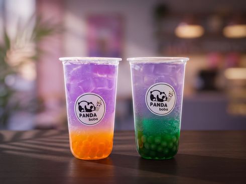 Two colorful bubble tea drinks in clear cups on a wooden table, with purple and orange layers and green tapioca pearls.