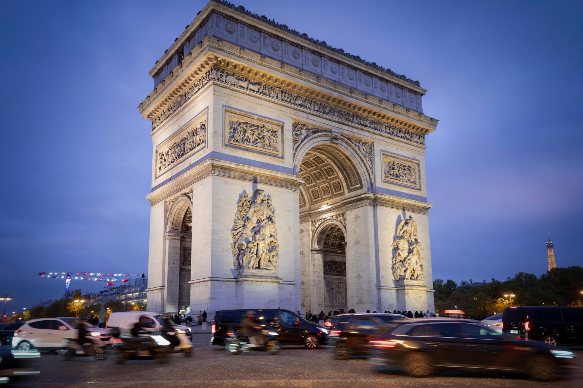 Arc de Triomphe in Paris at dusk, with traffic blurring in the foreground and a blue sky.