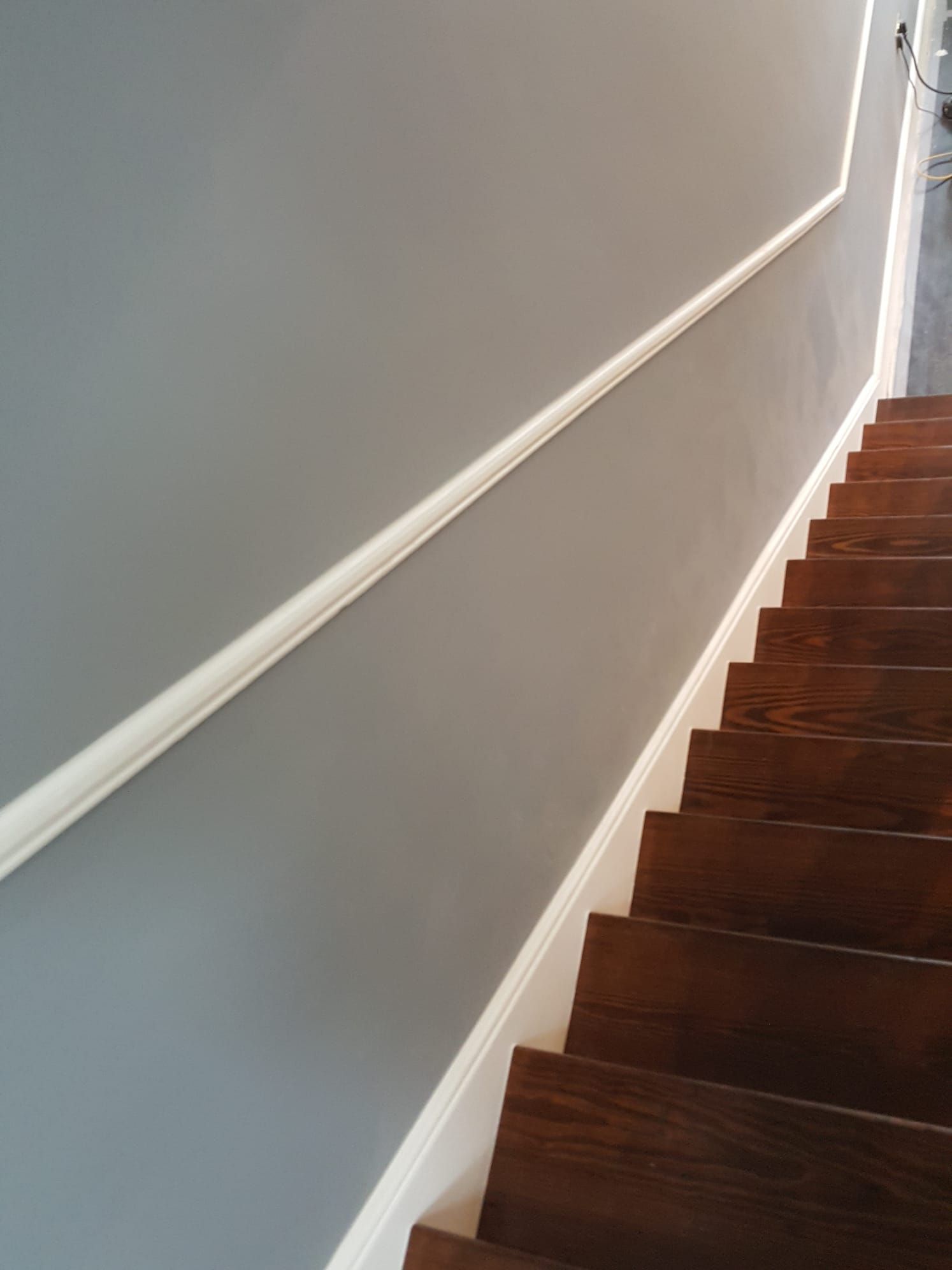 A wooden staircase with a white railing and a gray wall.