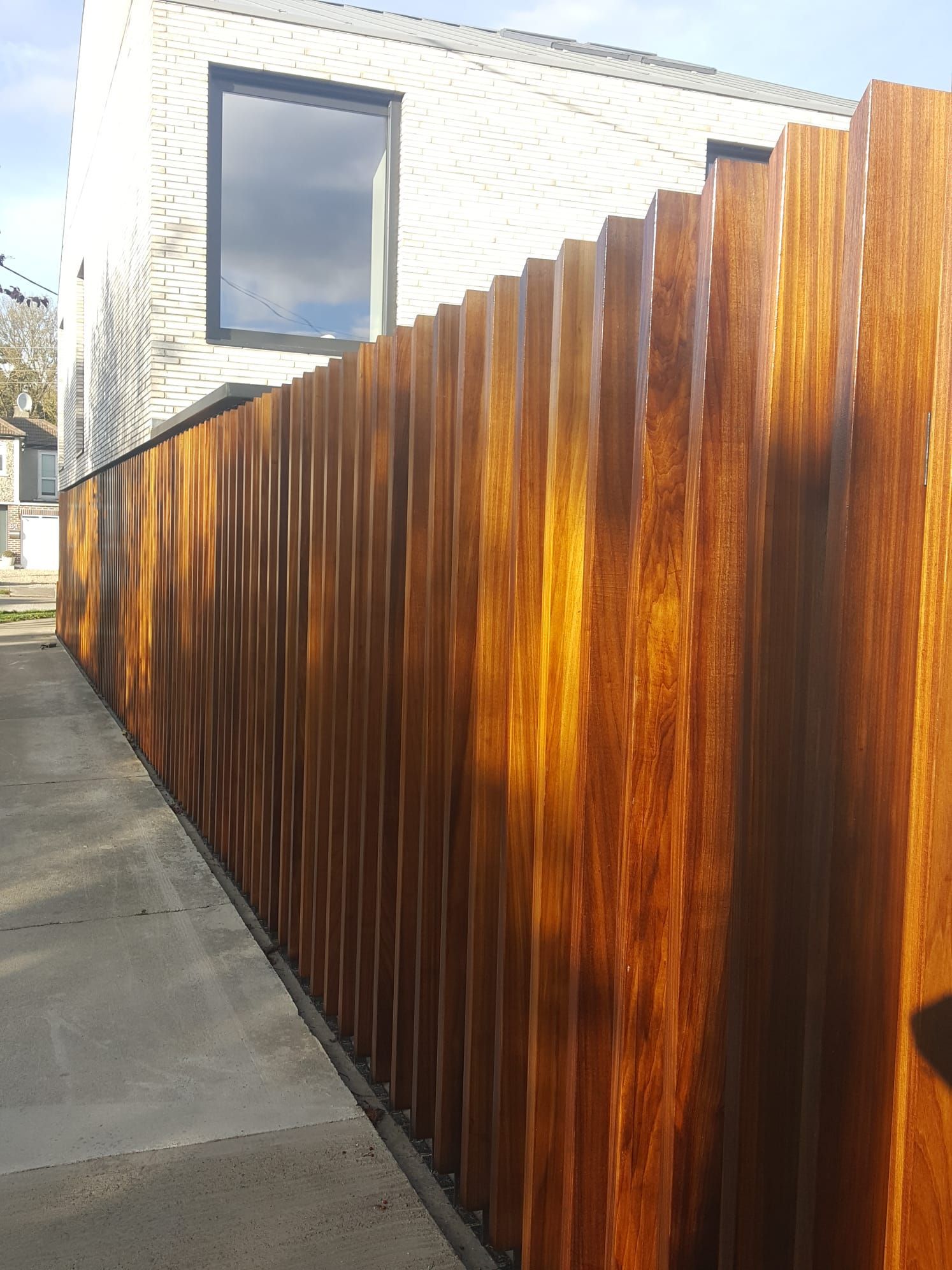 A wooden fence along a sidewalk in front of a white house.