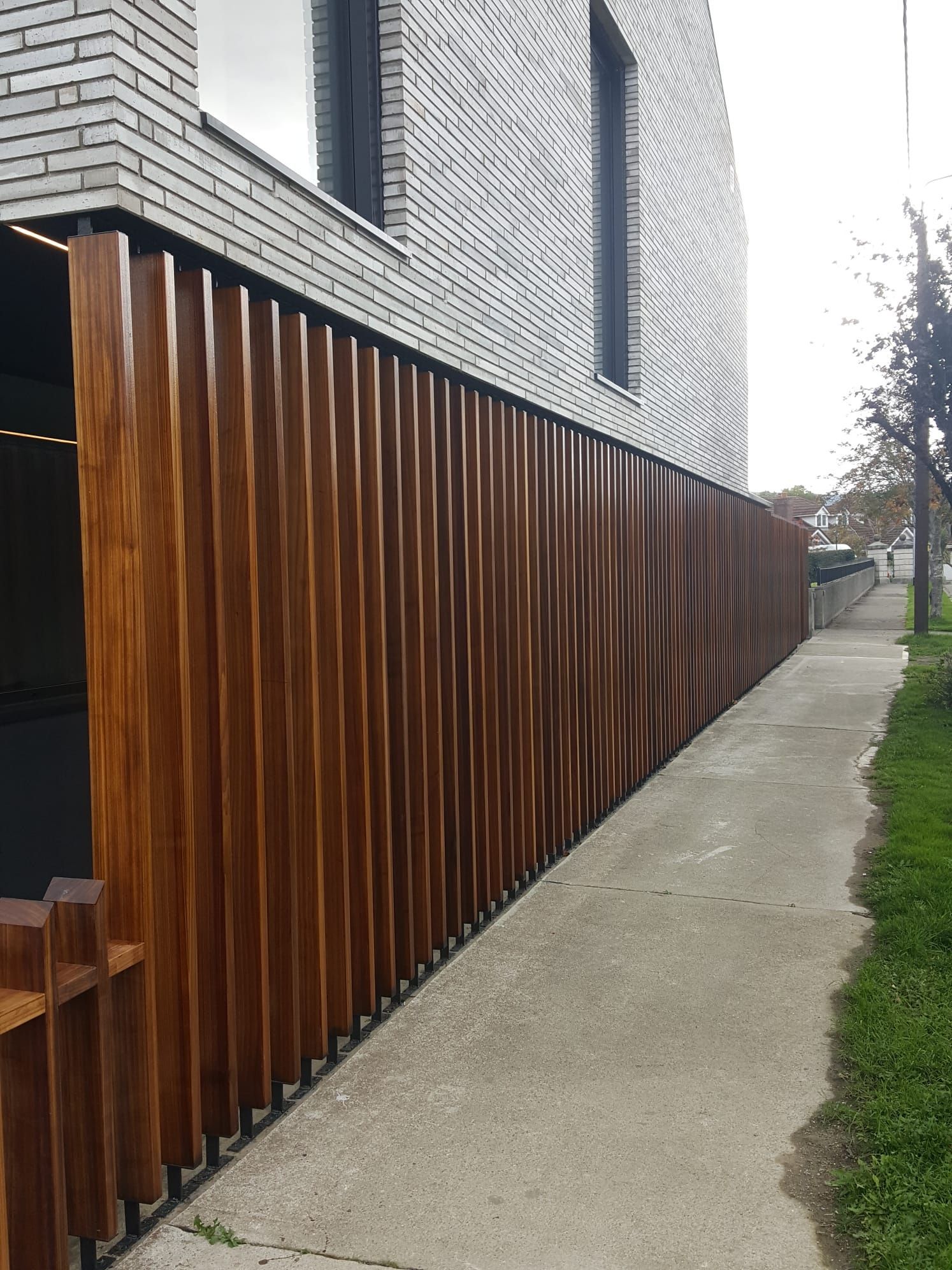 A wooden fence is along the sidewalk in front of a brick building.