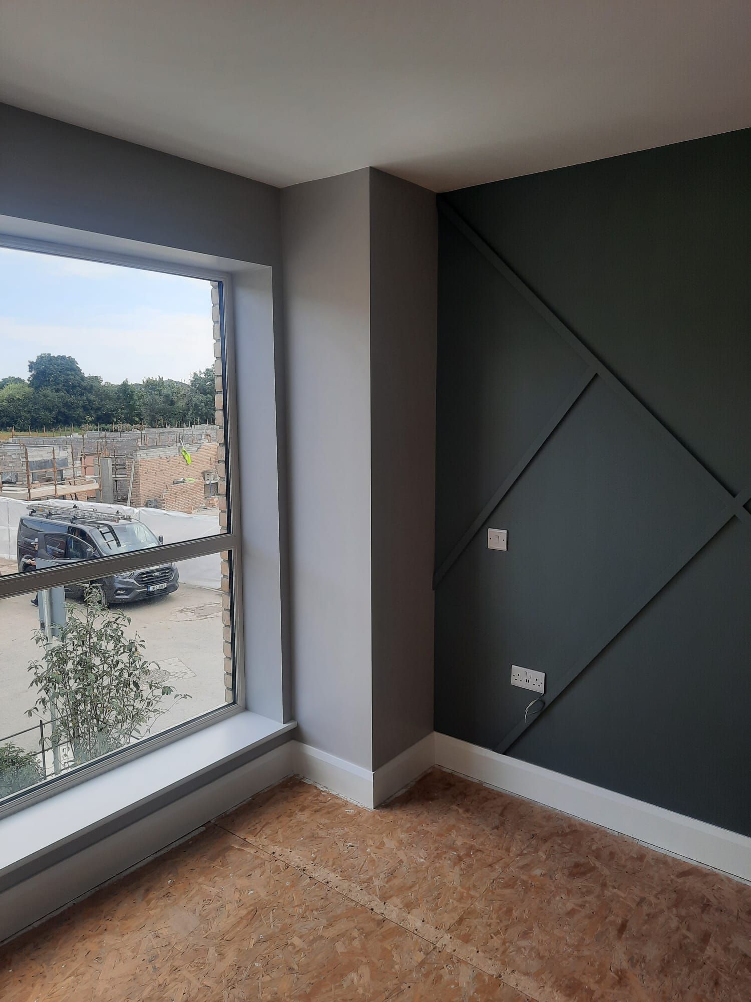 An empty room with a large window and a gray wall.