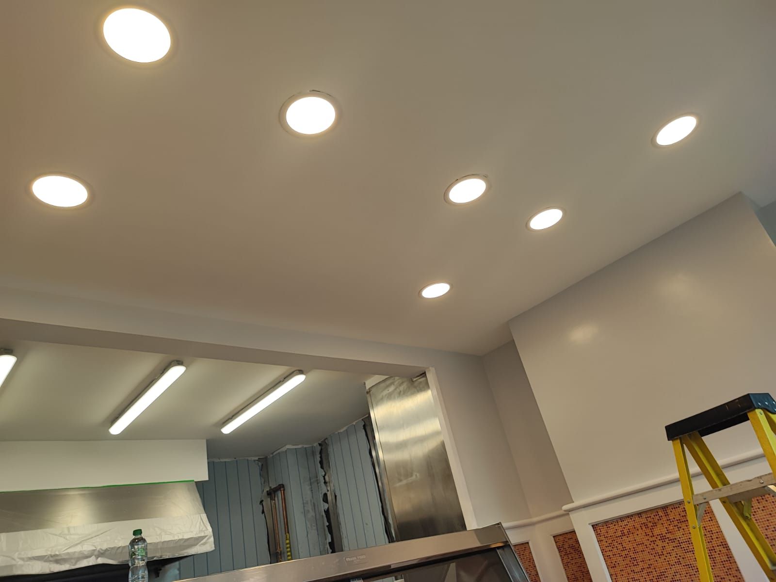 A kitchen with a lot of lights on the ceiling and a ladder.