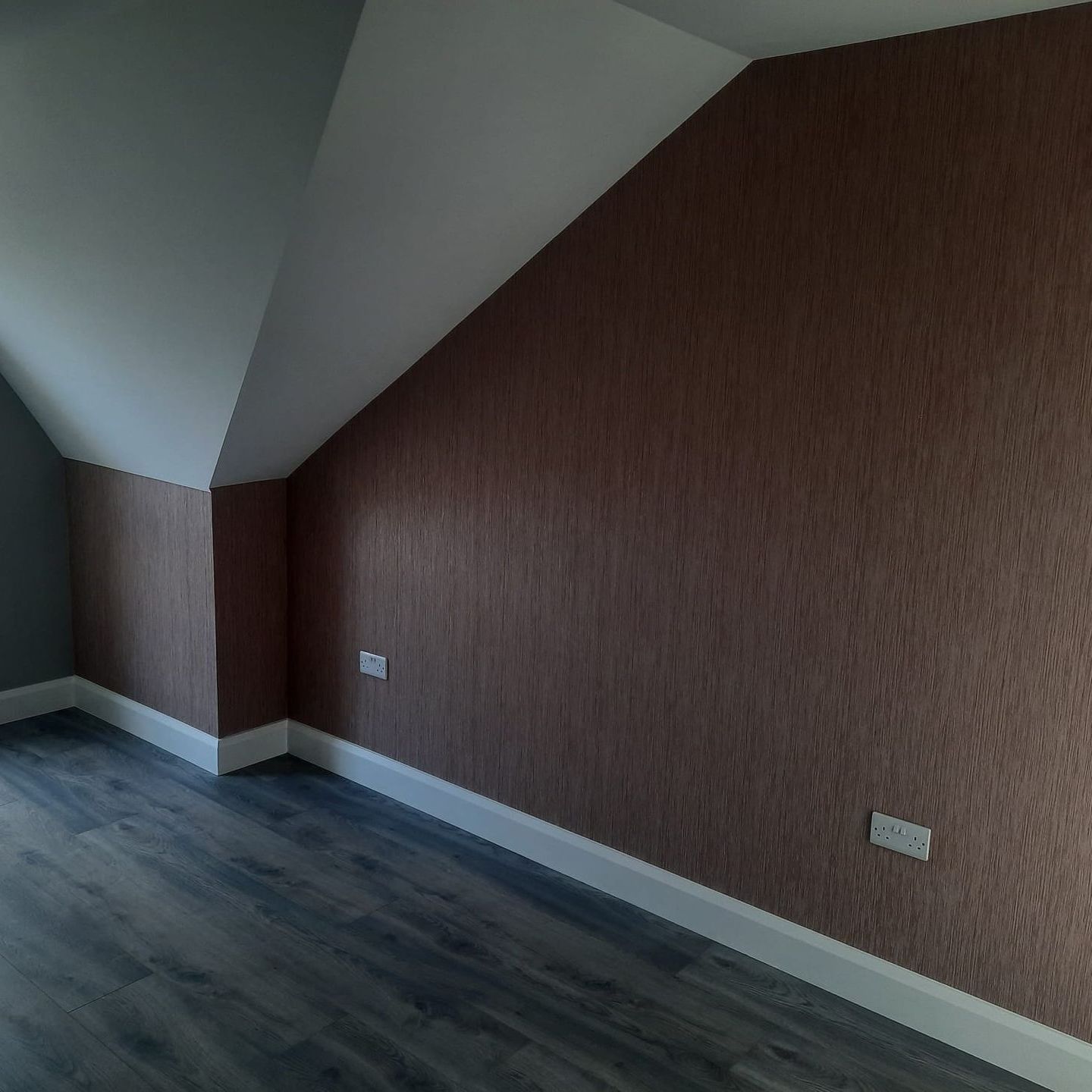 An empty room with a slanted ceiling and a wooden floor