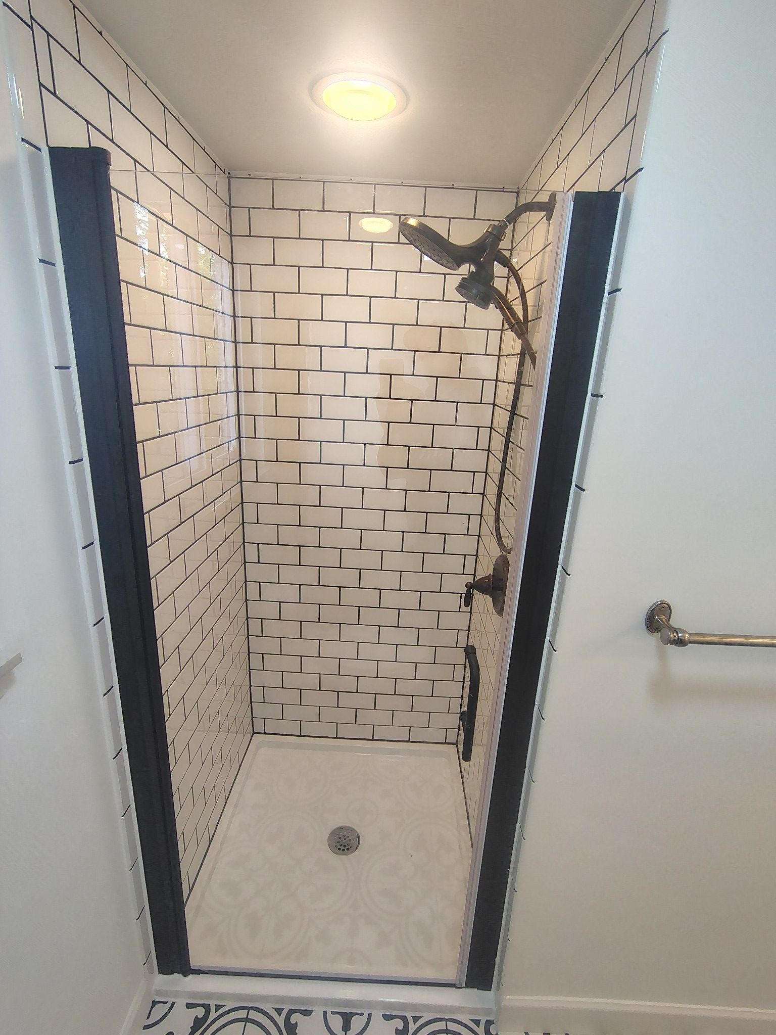 A modern shower with black trim, white subway tile walls, and a black showerhead.