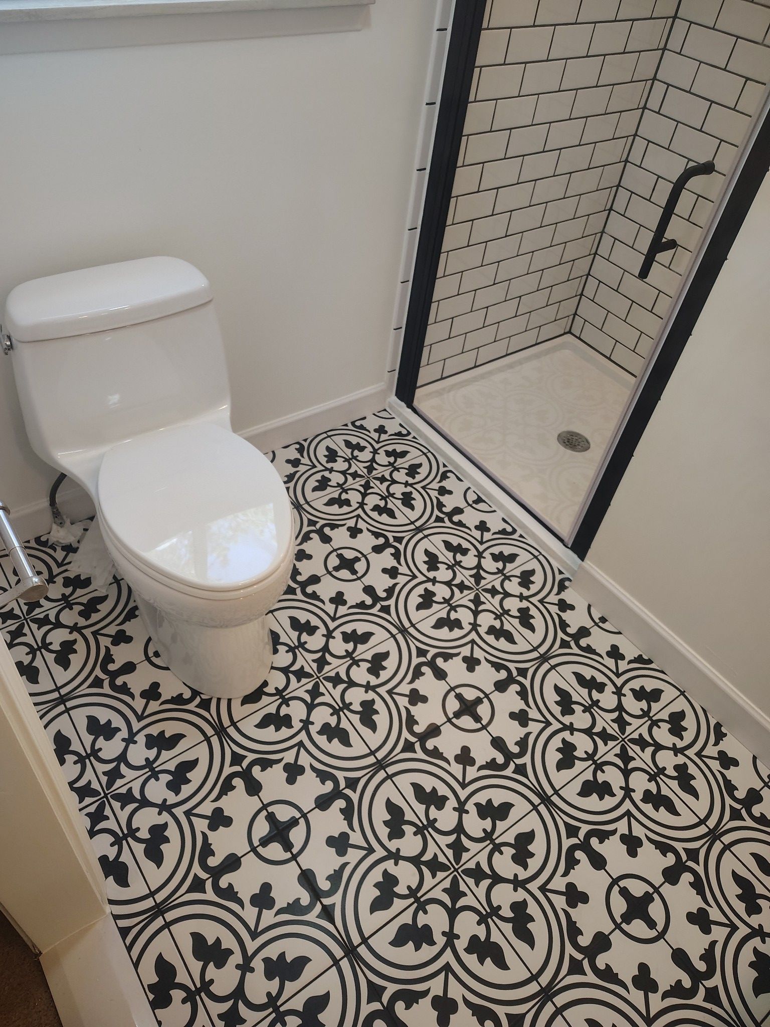 Bathroom with patterned black and white floor tiles, white toilet, and black-framed shower with white tile.