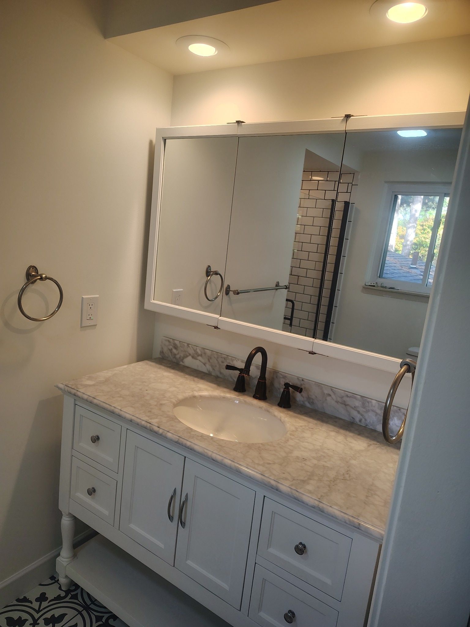 White bathroom vanity with marble countertop, mirror, and black faucet.