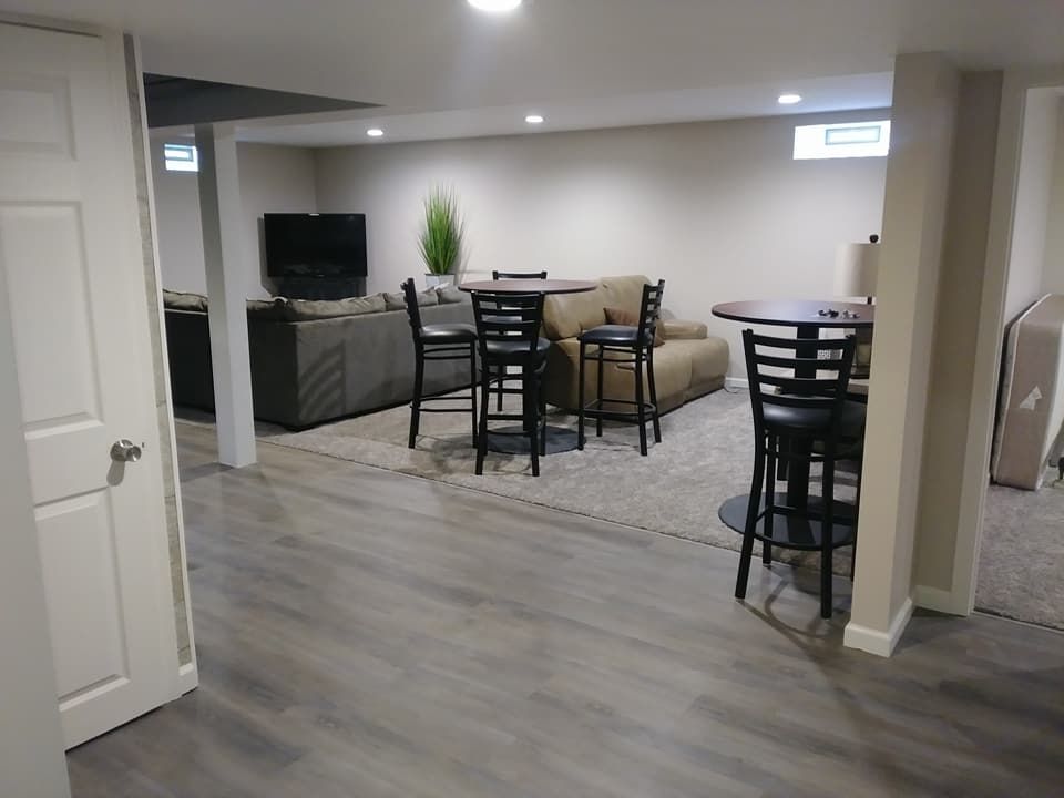 Basement with lounge area, tables, chairs, and television. Neutral colors. Flooring and recessed lighting.