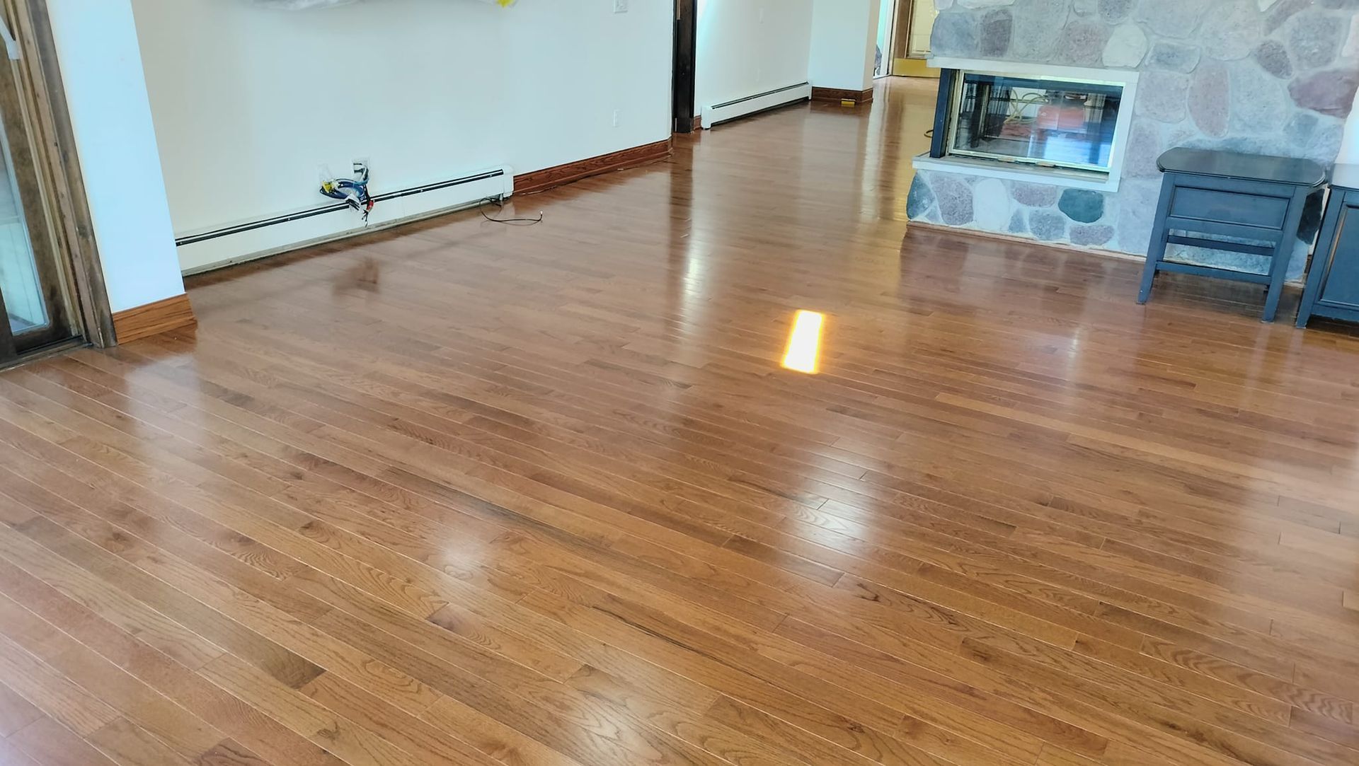 Reflective hardwood floors in a room with a stone fireplace, reflecting light.
