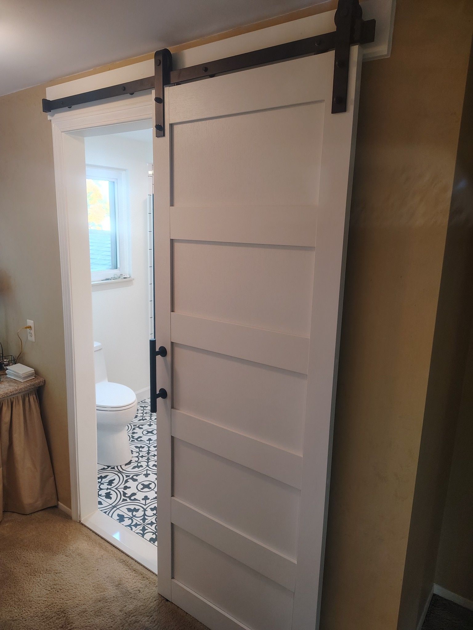 White barn door partially open to a bathroom with black and white patterned tile.