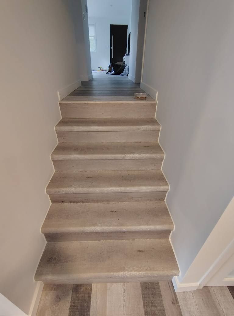 Staircase with gray wooden steps leading to a hallway with a dark door. White walls border stairs.